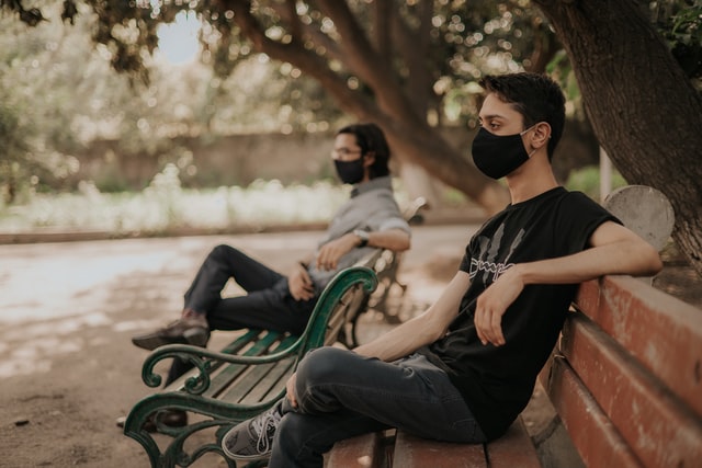 Two men sitting outside and wearing a mask while socially distancing