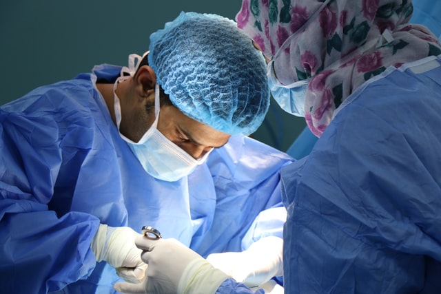 Two doctors wearing scrubs performing surgery on a patient