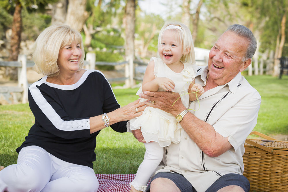 an elderly couple enjoying time with their granddaughter while picnicking outside