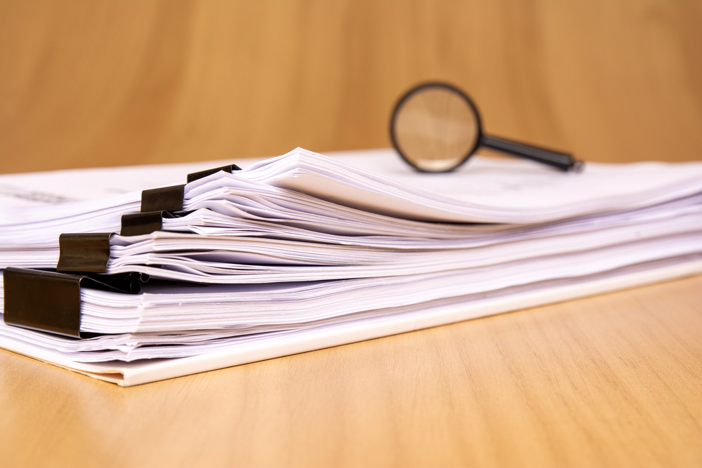 Stack of medical billing paperwork with magnifying glass, highlighting poor documentation